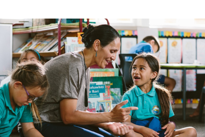 A teacher and their students sitting on the ground and discussing school work