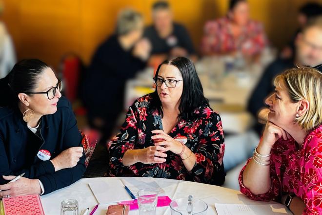 Three women talking around a table at a hui.